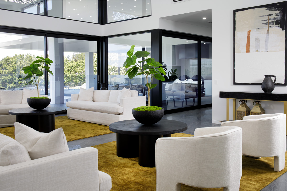 A bright, open living area with white sofas, gold rug and dark wooden furniture.