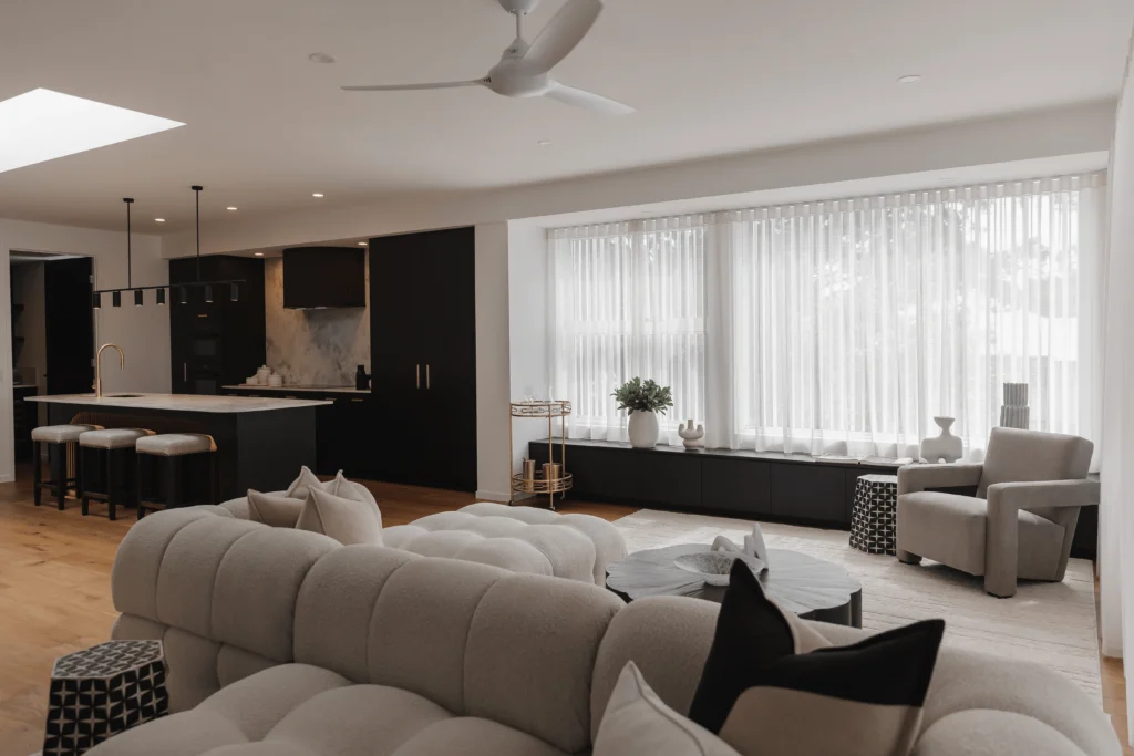 Modern open-plan living area showcasing luxury property styling with a plush tufted sofa, designer armchair, sleek black kitchen cabinetry, gold accents, and sheer curtains — creating a sophisticated and high-end interior.