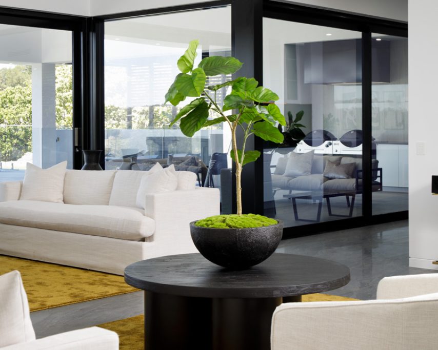 A light open plan modern living room with a gold carpet, dark tables, white sofas, and chairs.