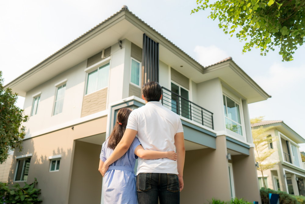 Young couple standing and hugging looking up at a house